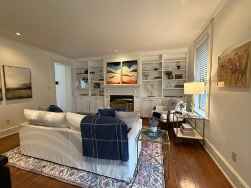Cozy living room with a white sofa, blue throw, shelves, and a fireplace.